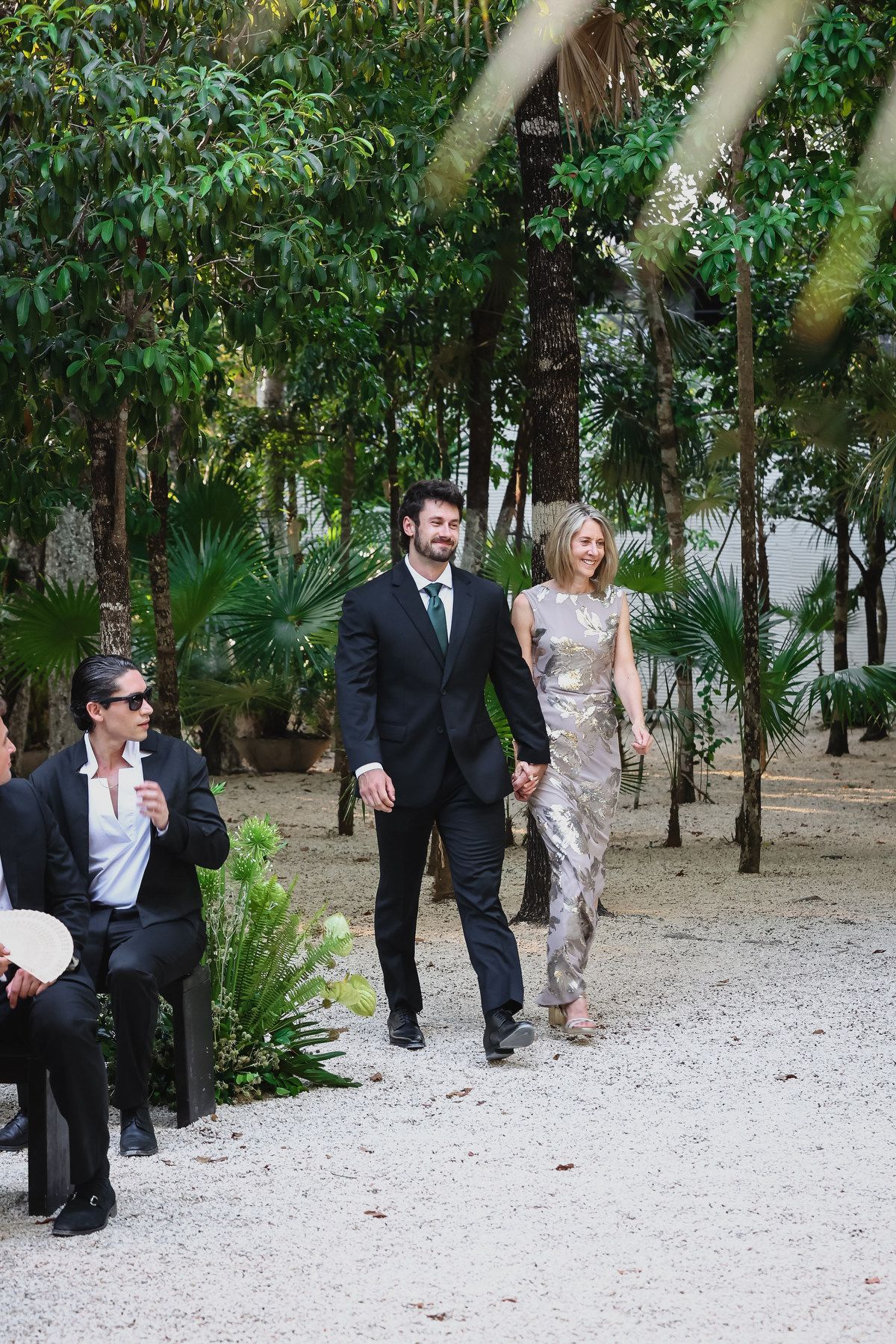Couple walks hand-in-hand through lush tropical garden at outdoor wedding ceremony.