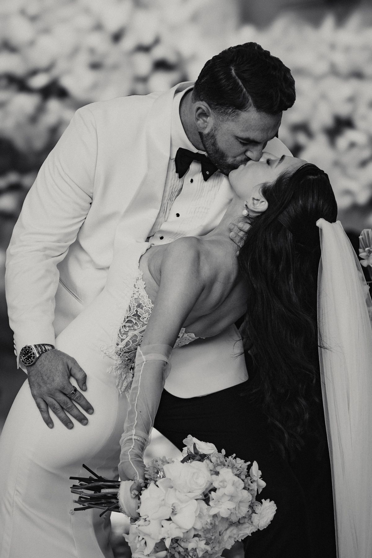 Black and white photo of bride and groom sharing a romantic kiss, bride holding a bouquet of white flowers.