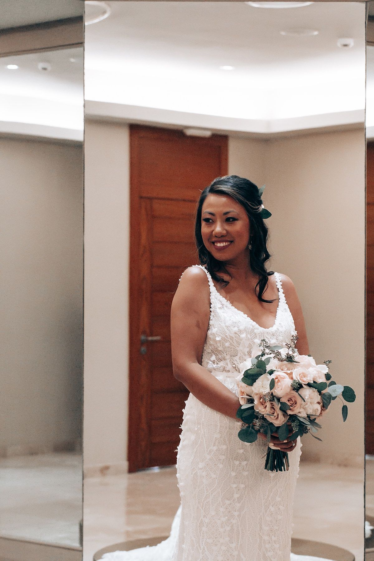Bride in a fitted lace wedding dress holding a peach and white bouquet.