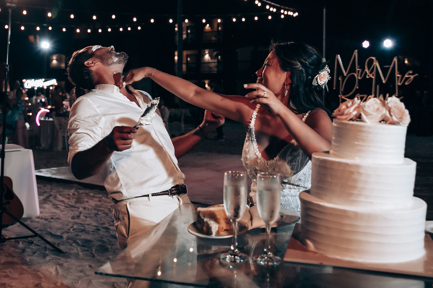 Wedding cake cutting ceremony at night with string lights creating an intimate ambiance.