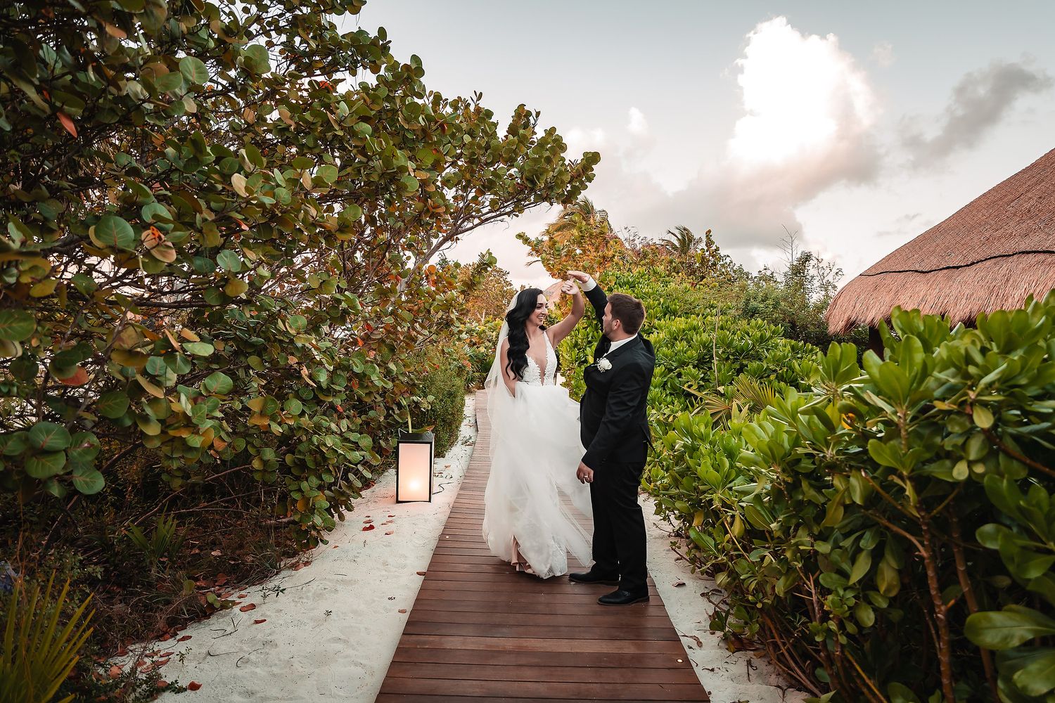 Bride and groom share a romantic moment on a wooden boardwalk surrounded by lush tropical greenery at a destination wedding.