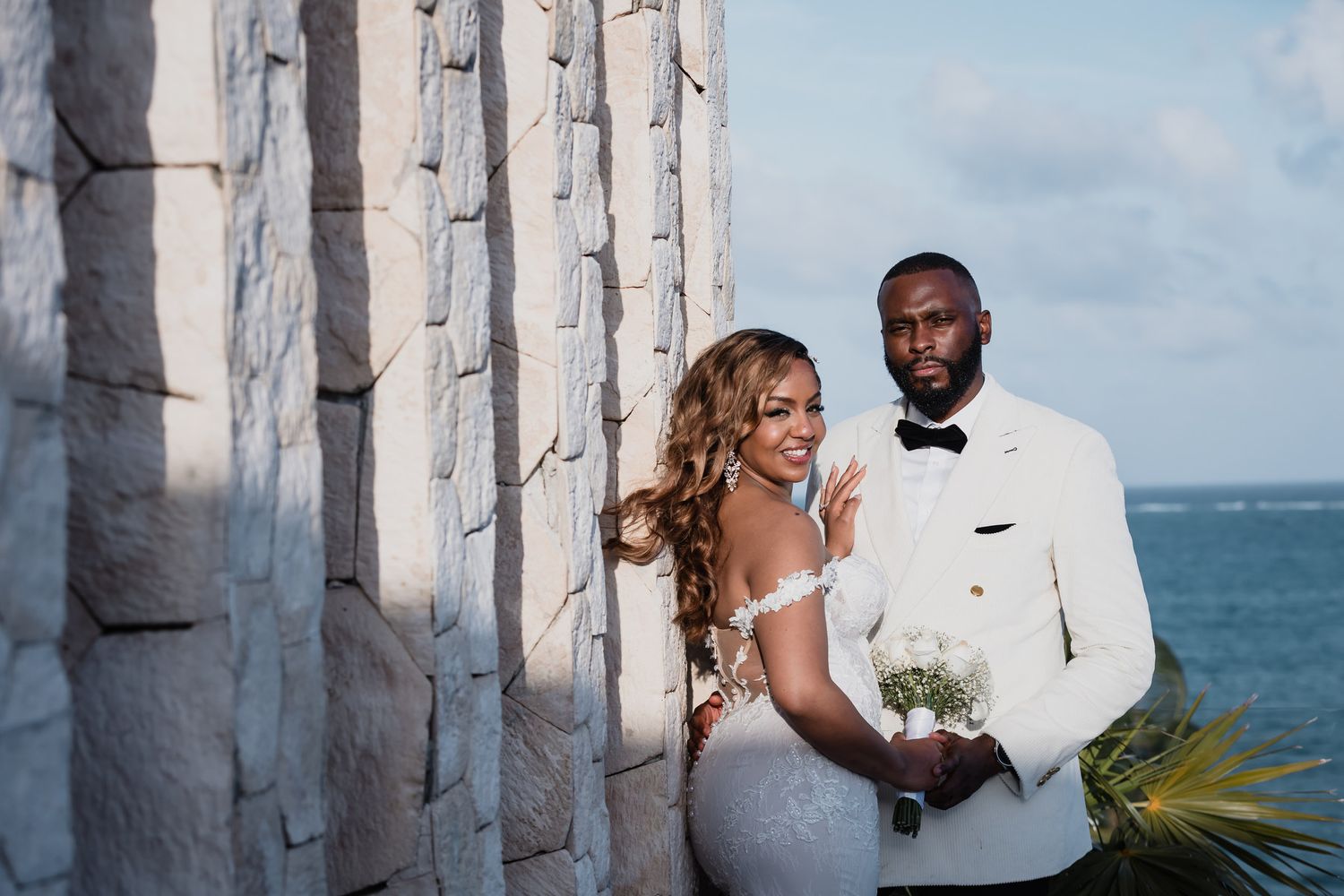 Bride and groom posing by stone columns with ocean view on their wedding day.