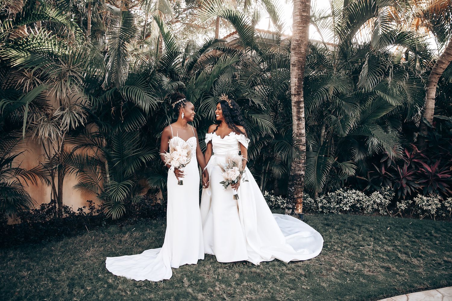 Wedding party poses among tropical palm trees in flowing white dresses.