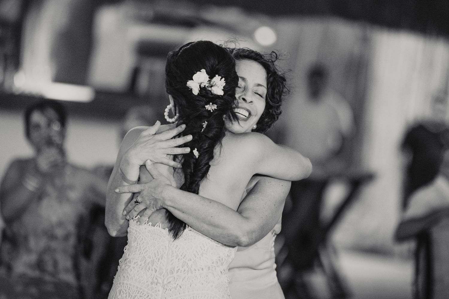 Black and white photo of bride sharing emotional hug with guest on wedding dance floor.