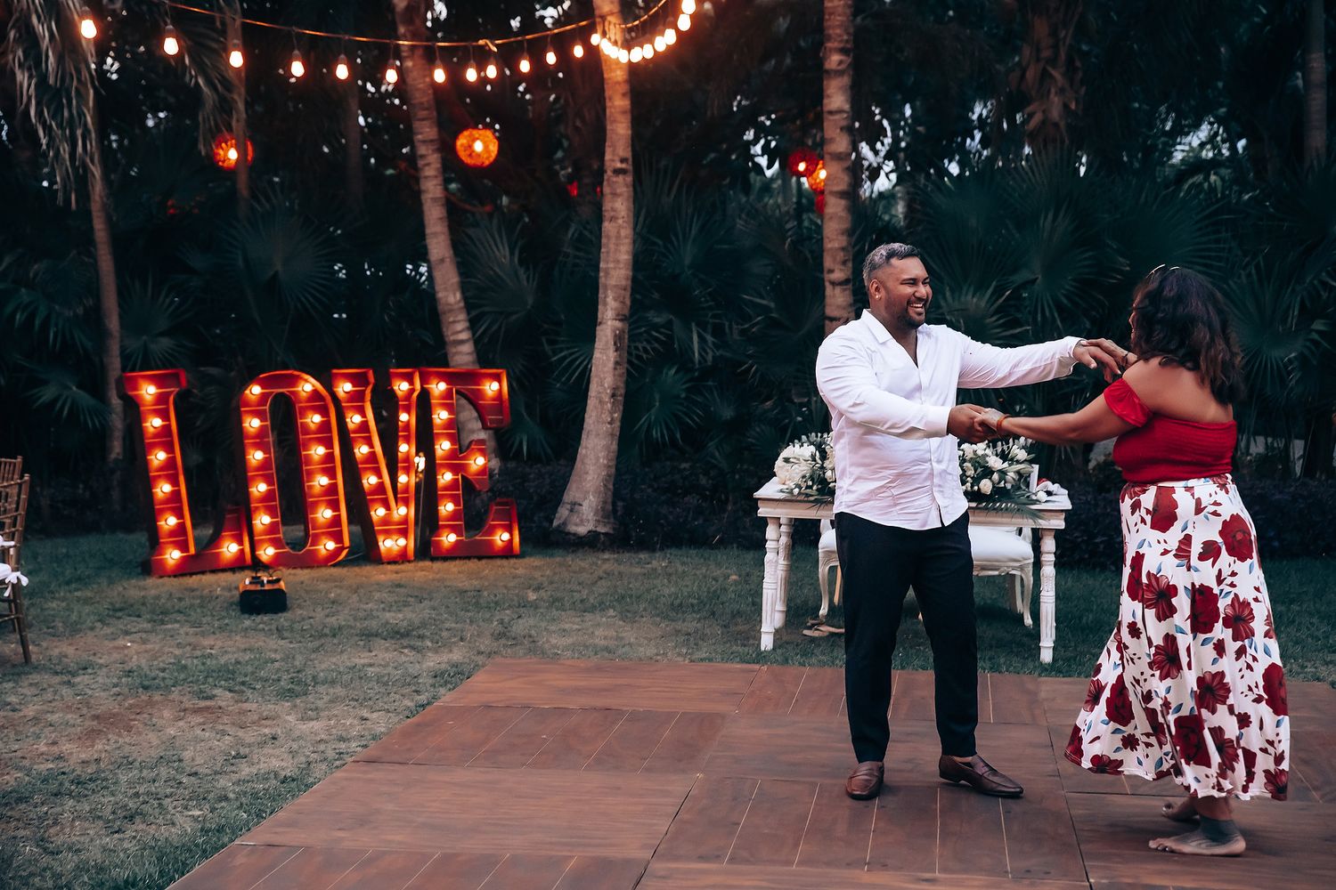 Wedding celebration at dusk with string lights illuminating an outdoor dance area surrounded by palm trees.