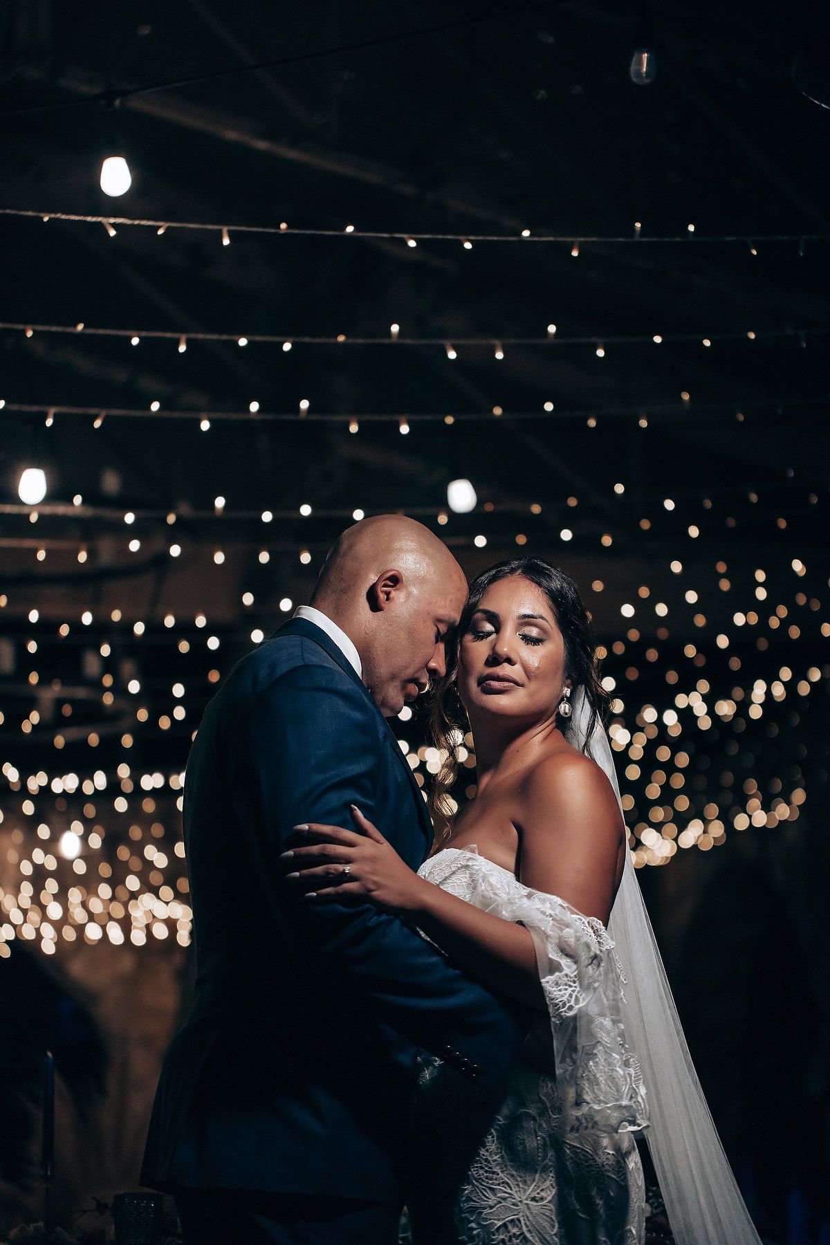 A couple shares an intimate dance moment under a canopy of string lights at their wedding reception.
