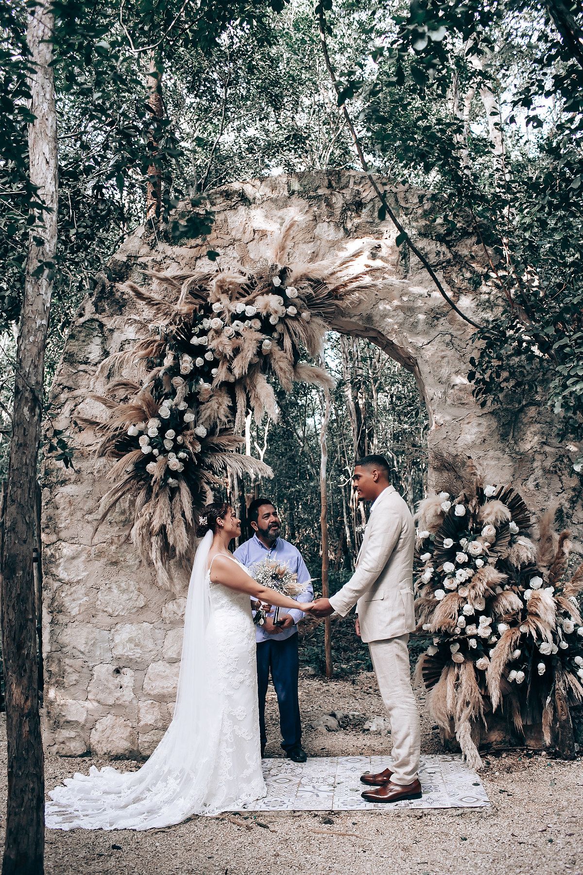 An intimate wedding ceremony takes place in a natural forest setting with stone backdrop.