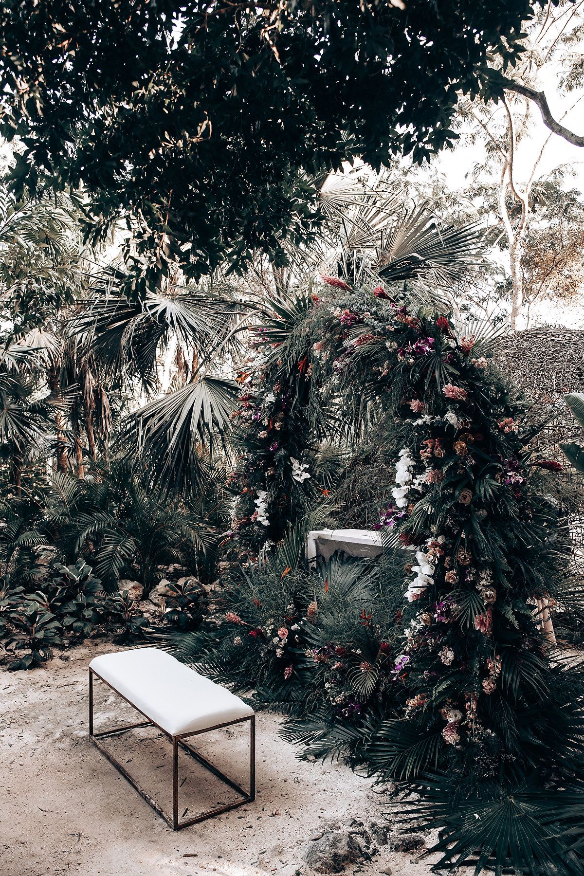 Modern white lounge chairs surrounded by lush tropical plants and palm fronds in an outdoor garden setting.