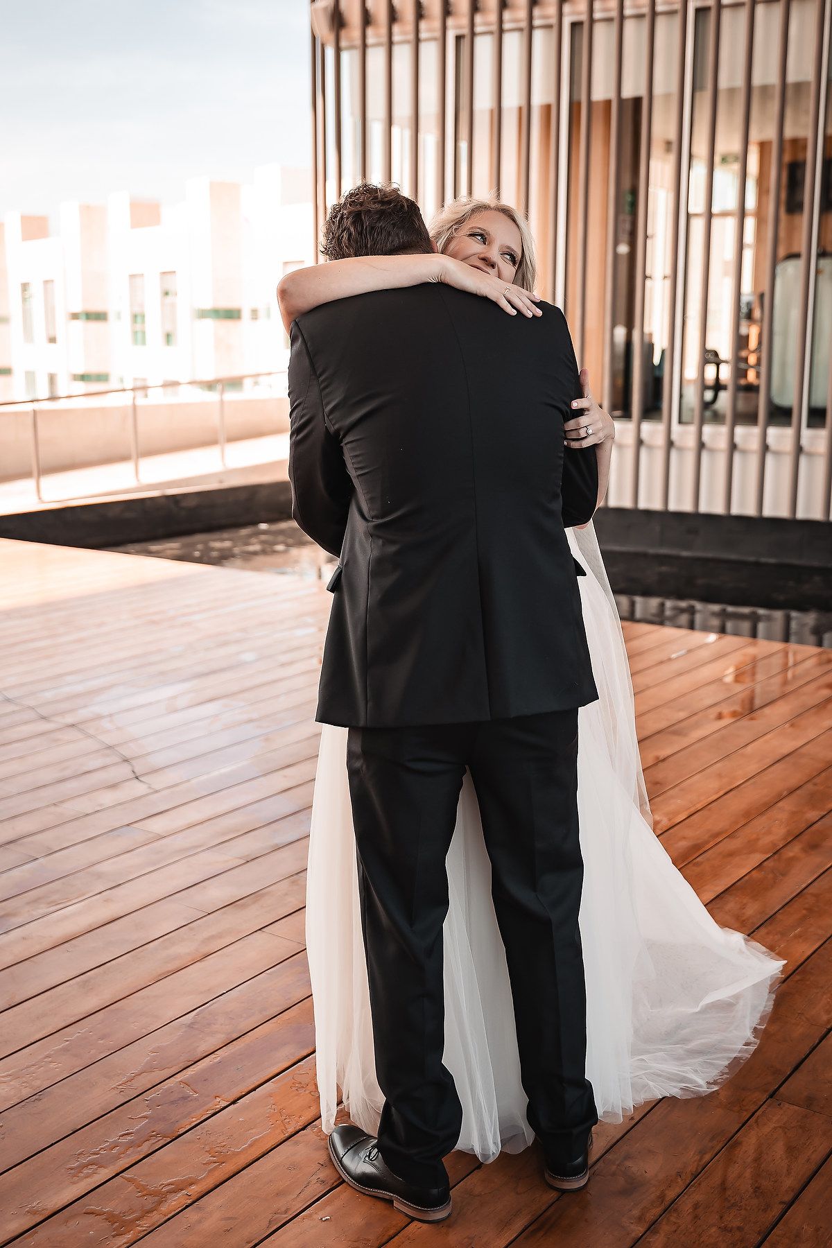 Intimate first look moment between newlyweds on a wooden deck with vertical railings.