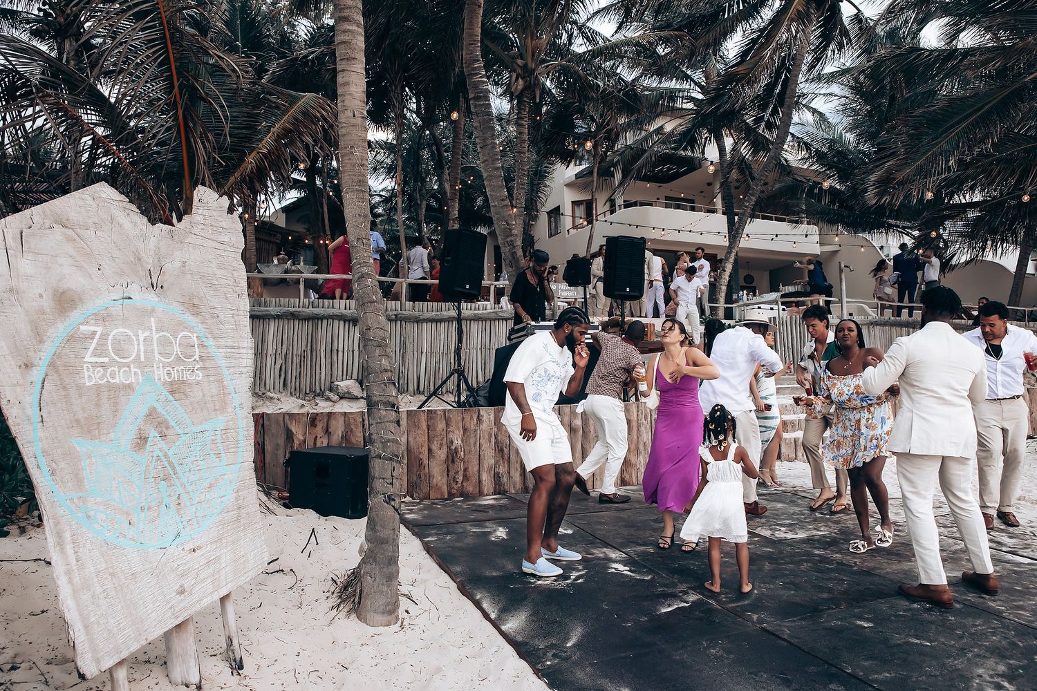 Wedding guests mingling under palm trees at a beachside reception.
