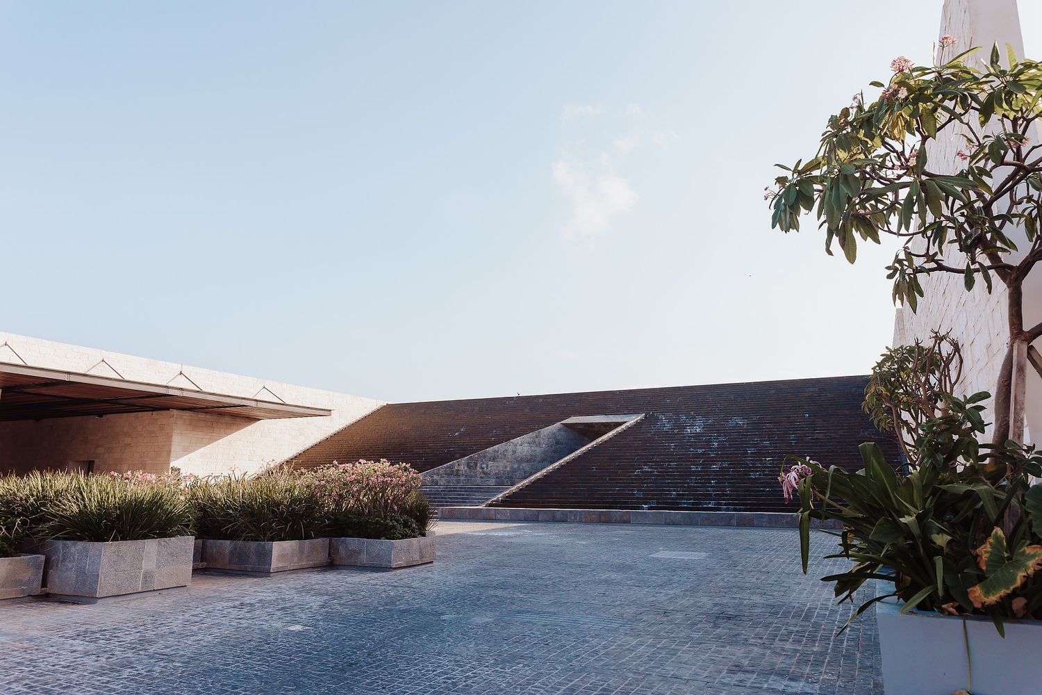 Modern architectural rooftop terrace with curved walls and landscaping against blue sky.
