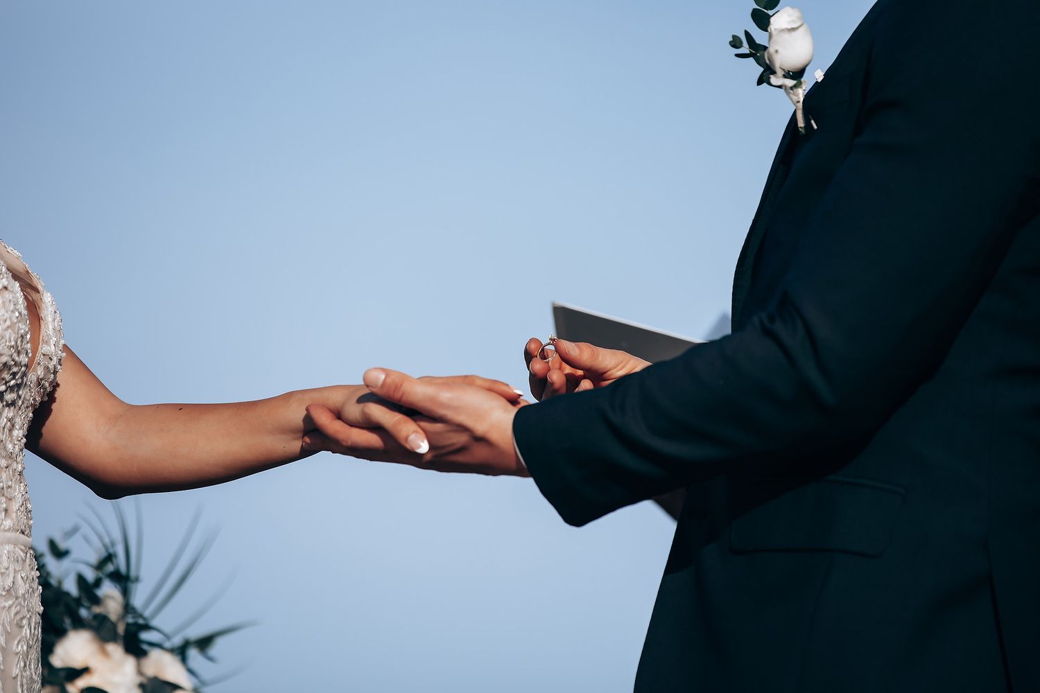 Close-up of hands during wedding ceremony exchange on tropical beach setting.