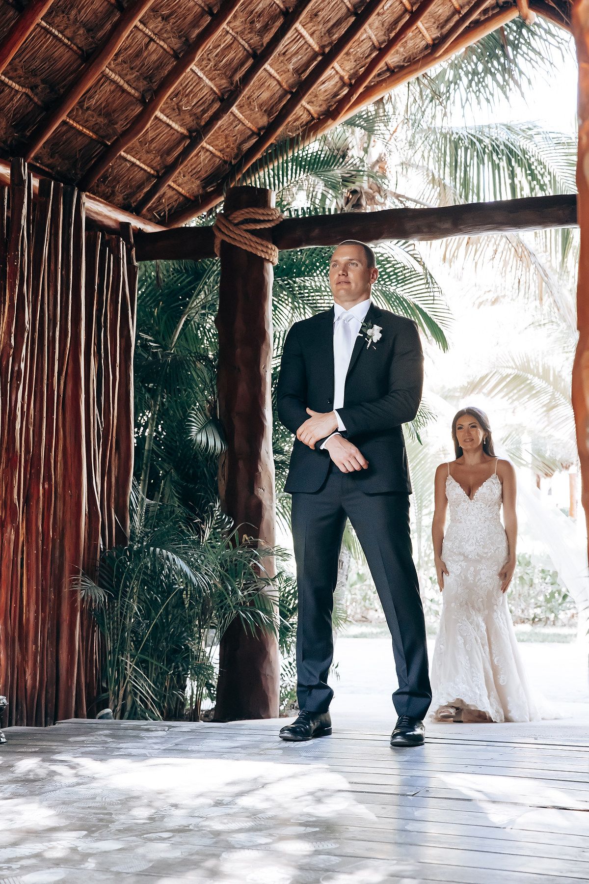 Couple dancing together under a rustic thatched-roof pavilion at a tropical beach wedding venue.