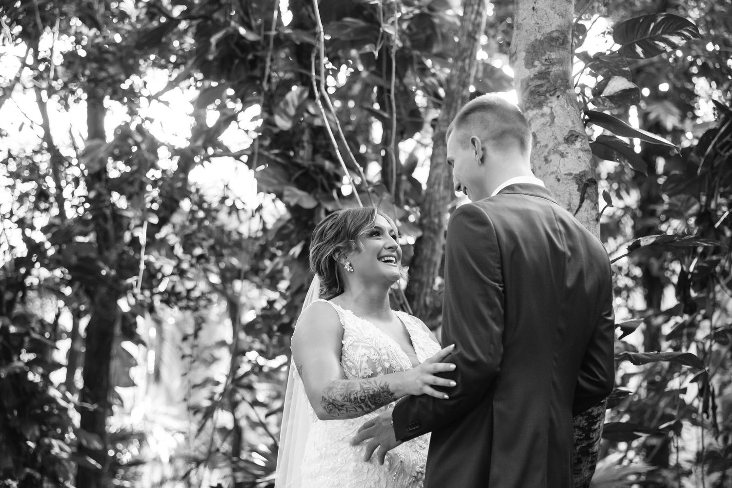 Black and white photo of a smiling bride and groom sharing a tender moment during their outdoor forest wedding ceremony.