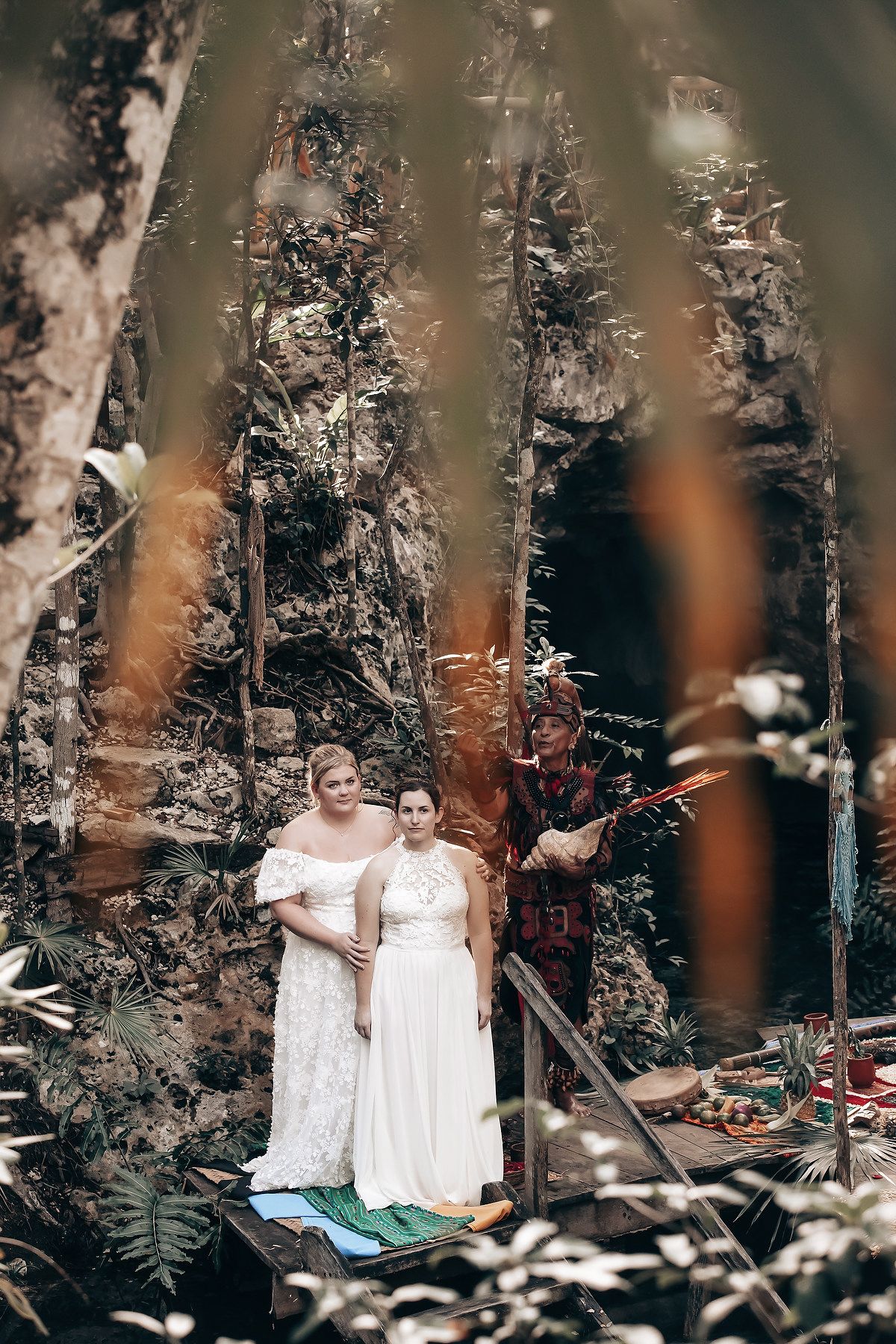 Two people in wedding attire standing in a lush, forested environment with various decorative elements.
