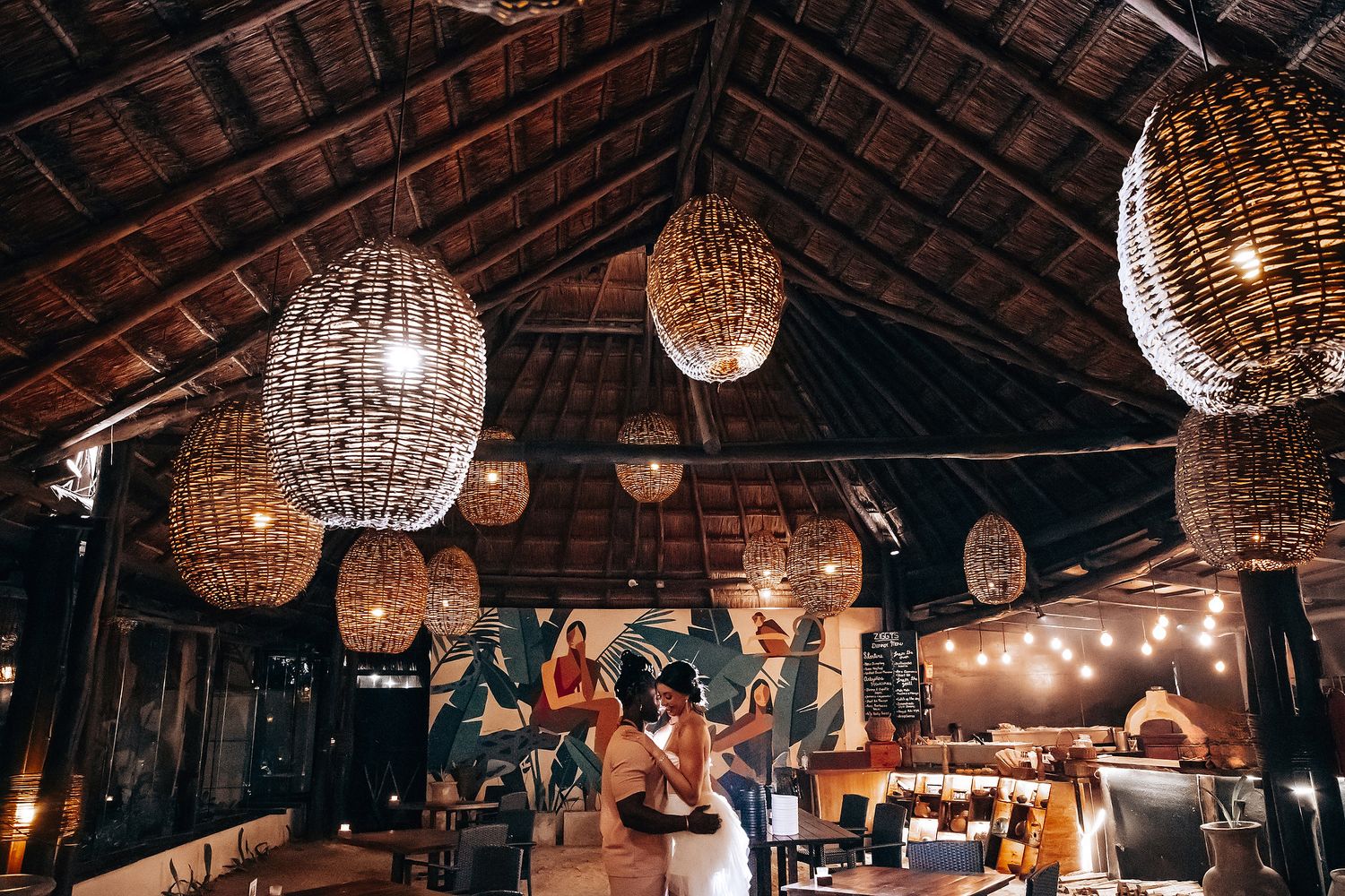 A cozy indoor space with hanging woven light fixtures and people gathered around.
