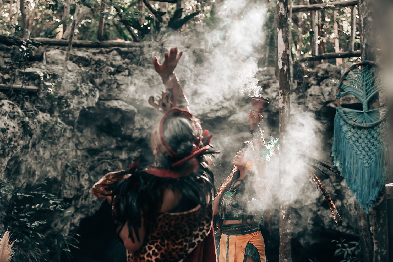 A couple stands together in a tropical forest setting, with a person in traditional dress nearby.