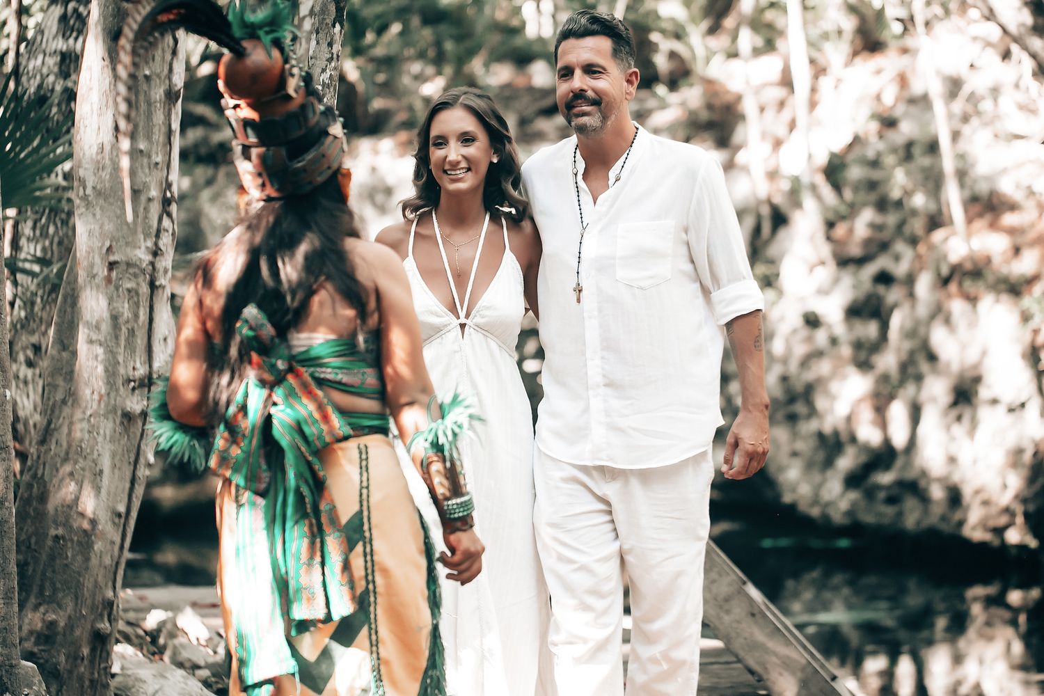 A couple walking together in a lush, natural setting, the woman wearing a colorful dress and the man in a white shirt.