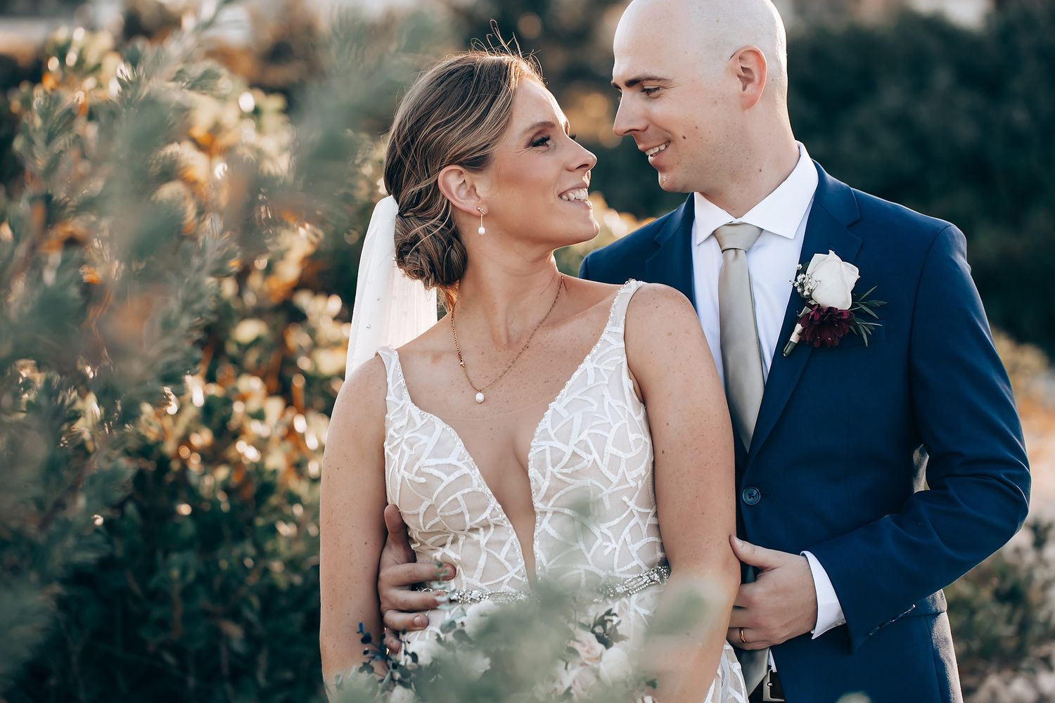 A bride and groom embracing and posing for a photograph in a beautiful natural setting.