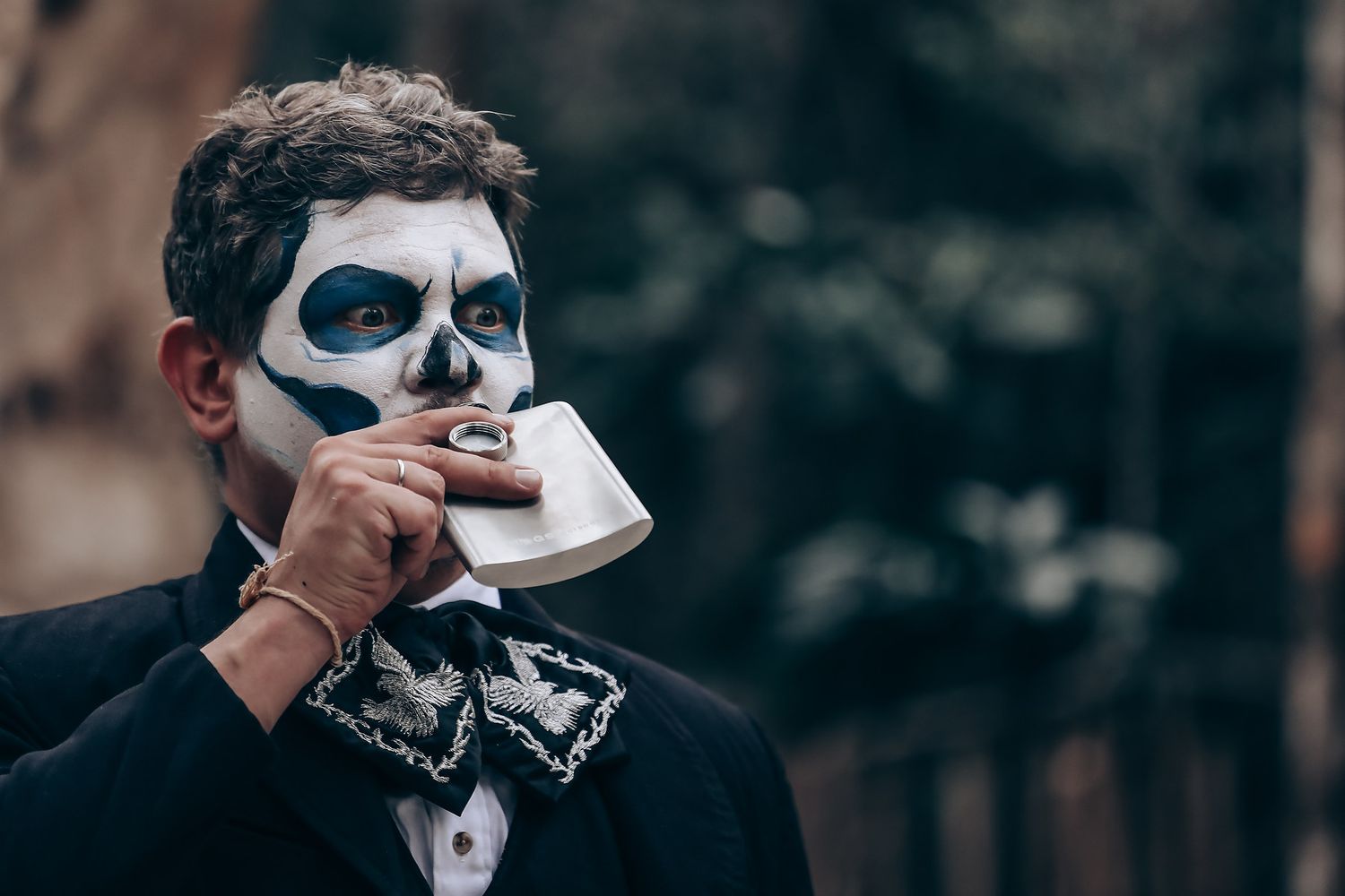 Person with Day of the Dead face paint sips from a teacup at outdoor event.