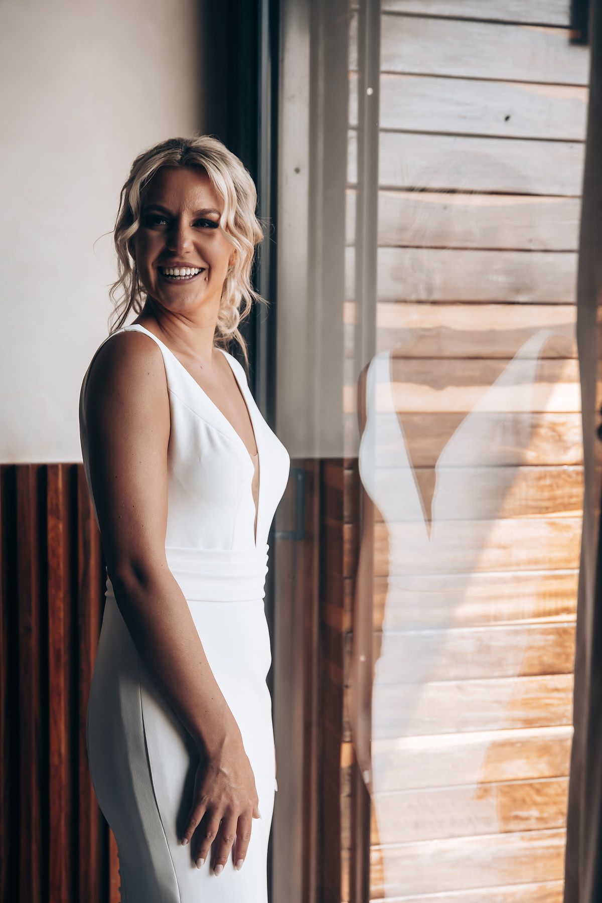 White wedding dress detail shot against rustic wooden wall with natural lighting.