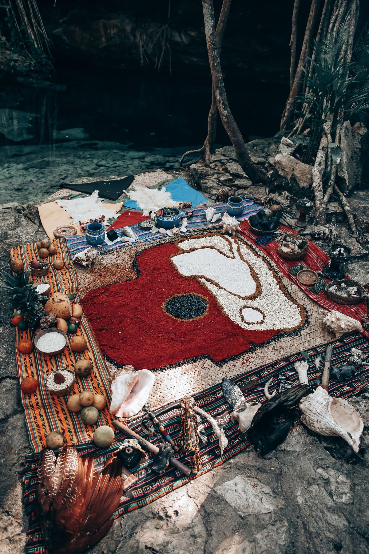 A rustic outdoor setup with red and white rugs and wooden furniture arranged in a forest setting.