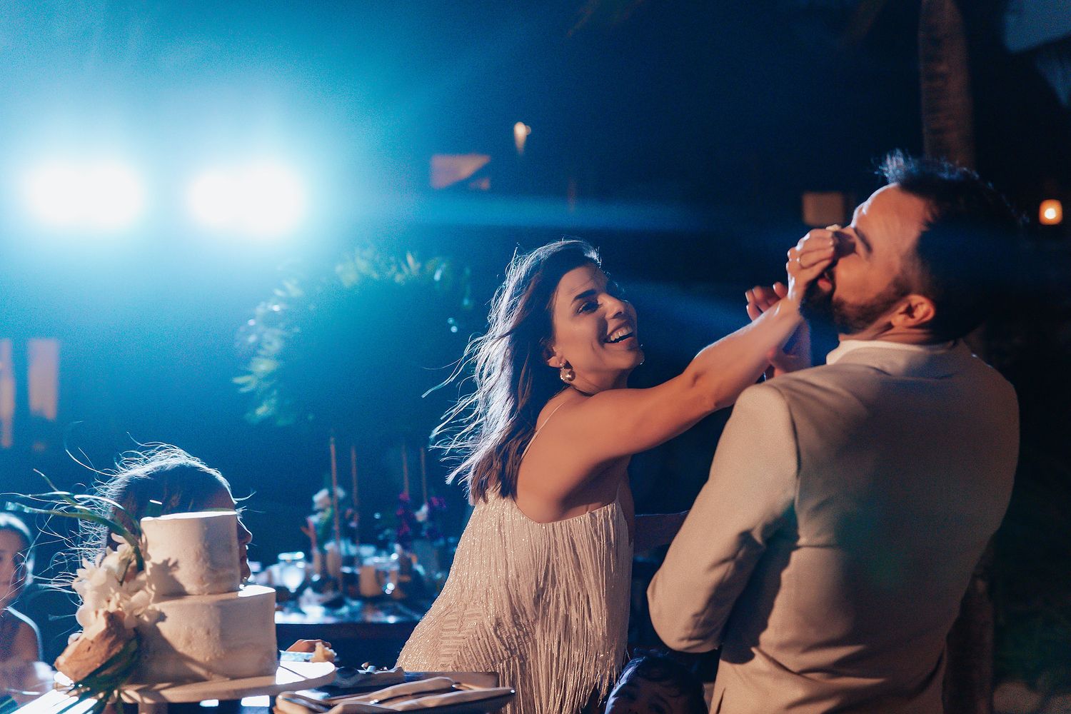 Wedding guests dancing and celebrating under blue evening lighting at an outdoor reception.