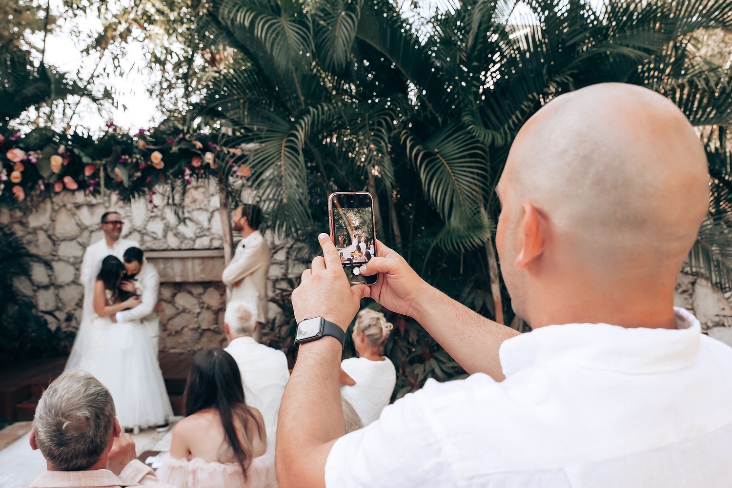 Wedding guests watching and taking photos during an outdoor ceremony.