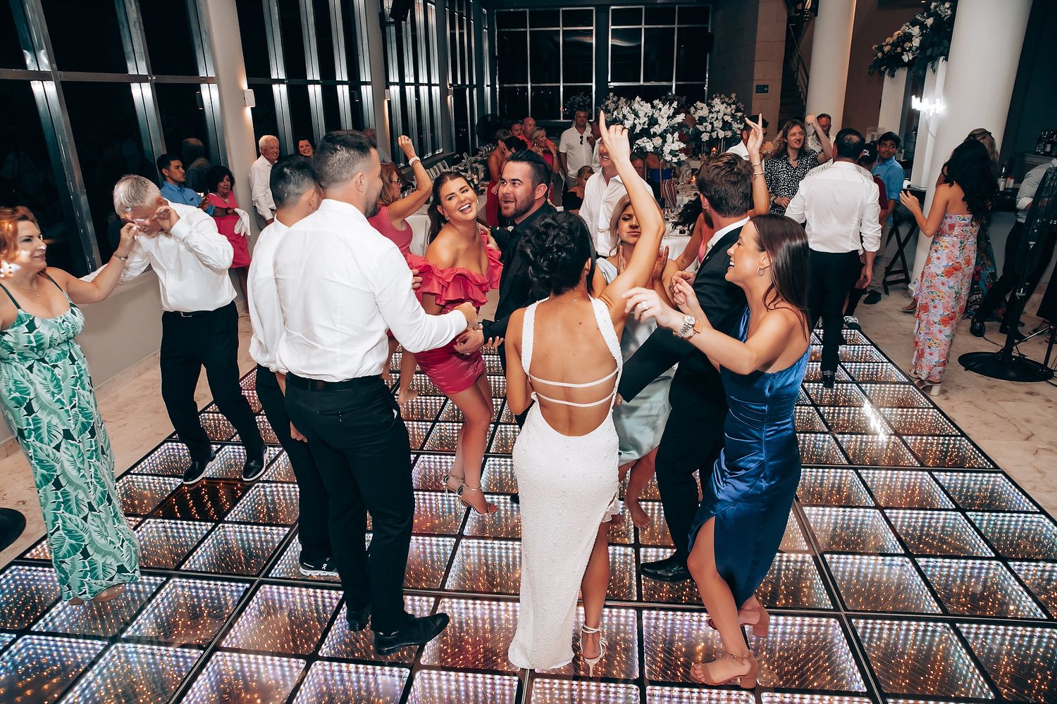 Guests enjoying themselves on a lit-up dance floor during wedding reception celebration.