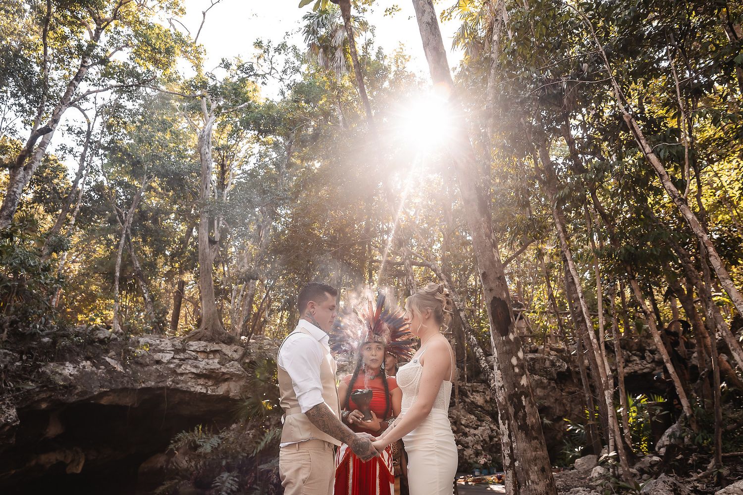 Couple exchanges vows with officiant in sunlit forest during intimate woodland wedding ceremony.