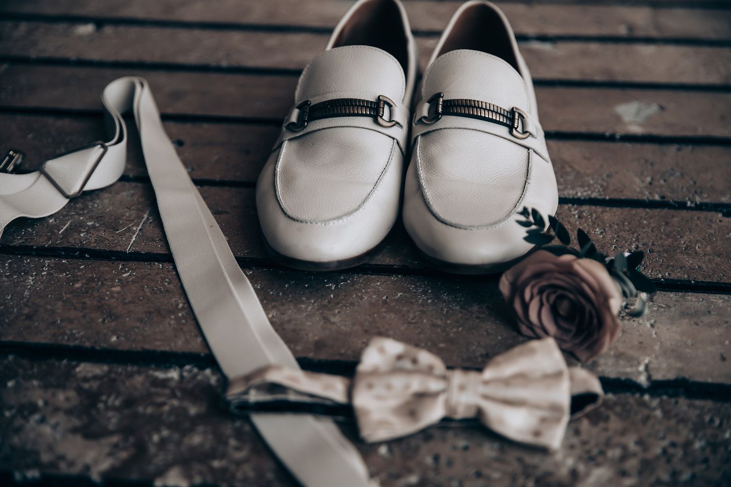White wedding shoes and accessories arranged on dark wooden deck.