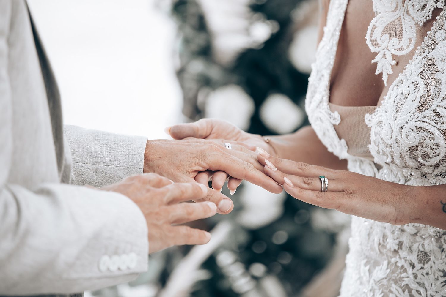 Close-up of hands exchanging wedding rings during ceremony with lace dress detail.