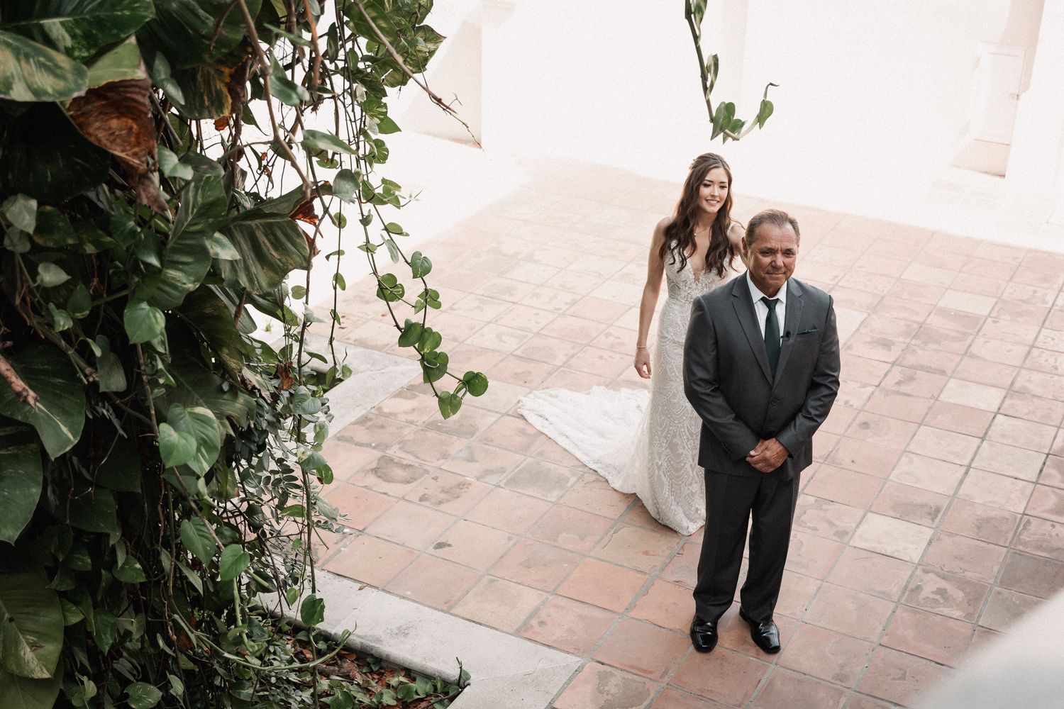 Aerial view of bride in white lace gown and groom in gray suit at outdoor garden wedding venue.