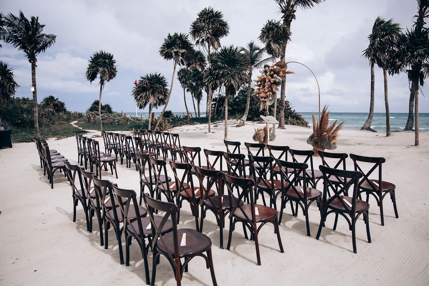 Wooden cross-back chairs arranged in rows on beach for destination wedding ceremony.