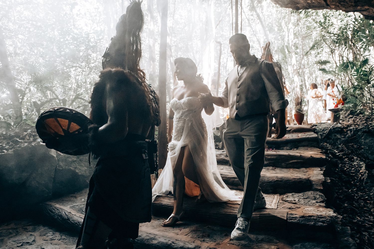 Atmospheric photo of people walking up misty stone steps in a dreamy forest setting with soft sunlight filtering through.