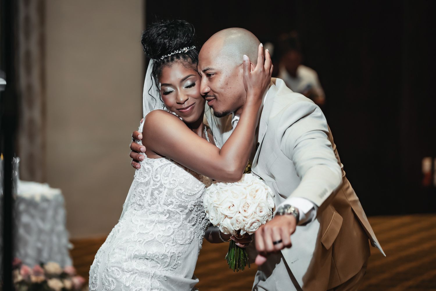 Bride and groom sharing a joyful embrace at their wedding reception, bride holding white bouquet in elegant lace gown.