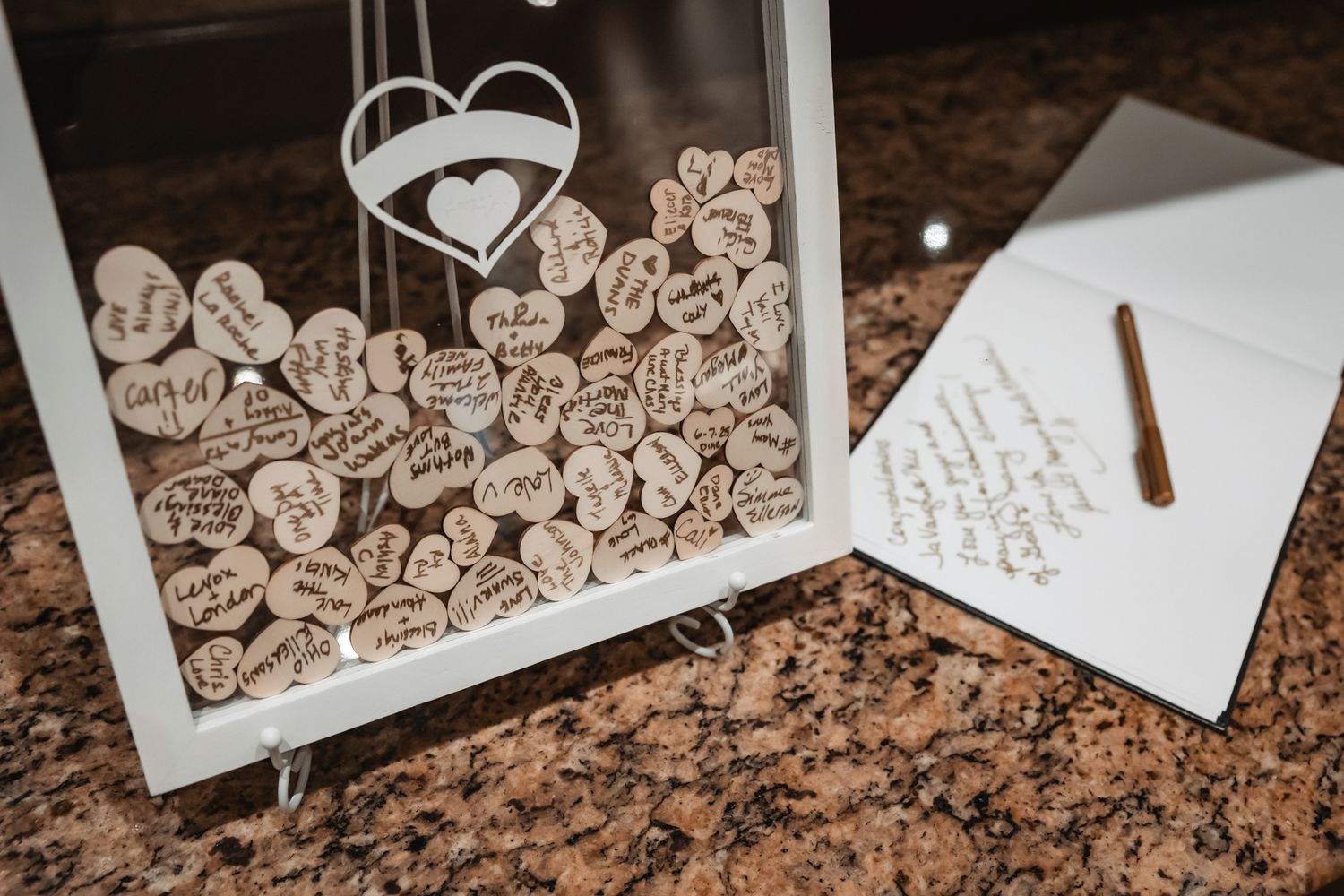 Rustic wedding guest book shadow box filled with wooden heart-shaped tokens and messages, displayed beside a notepad and pen.