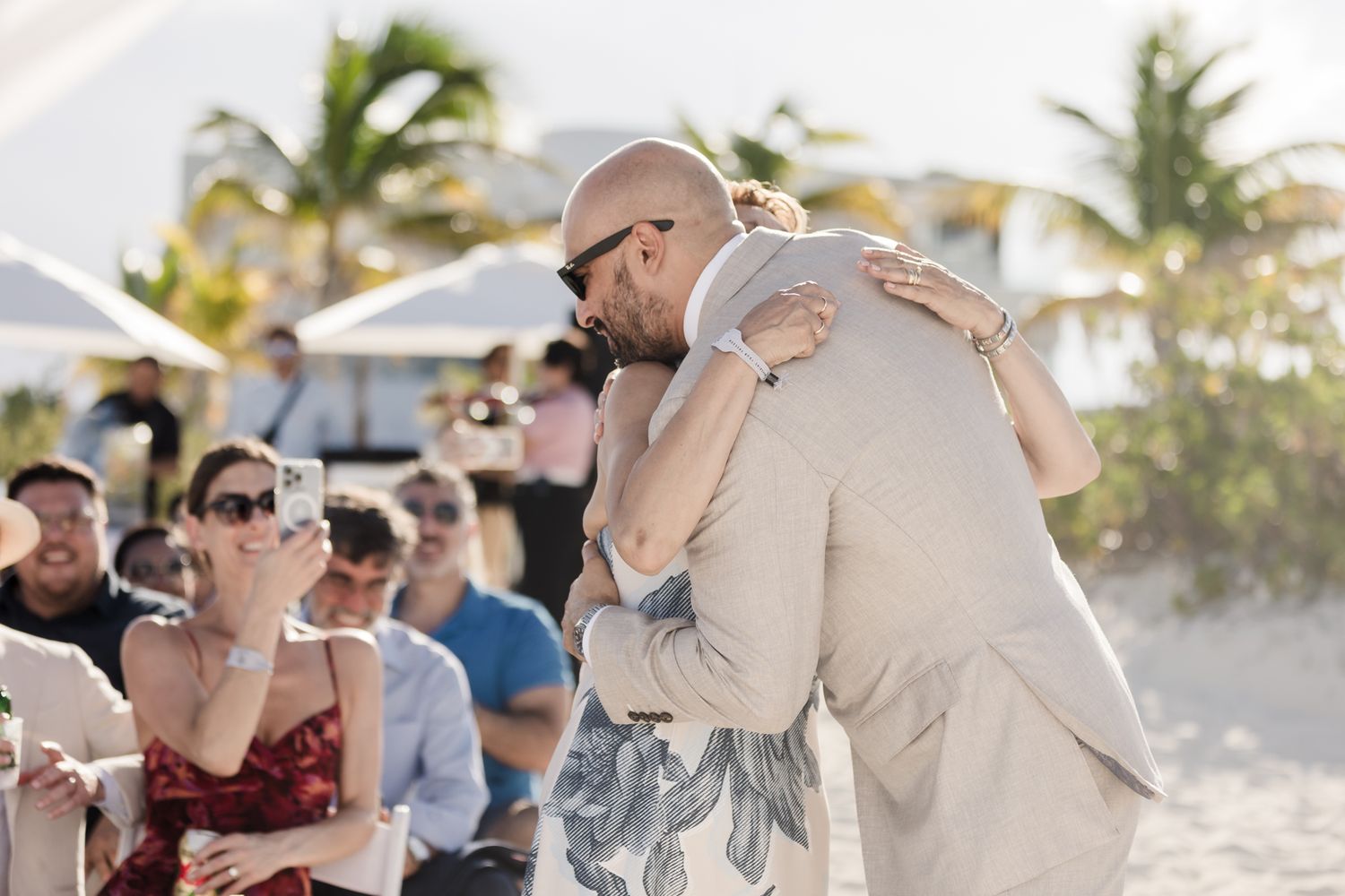 Couple sharing an emotional hug during a beach wedding ceremony with guests watching in the background.
