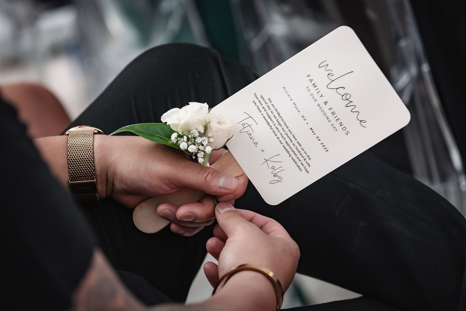 Close-up of hands holding a wedding program with a white floral wrist corsage during a ceremony.