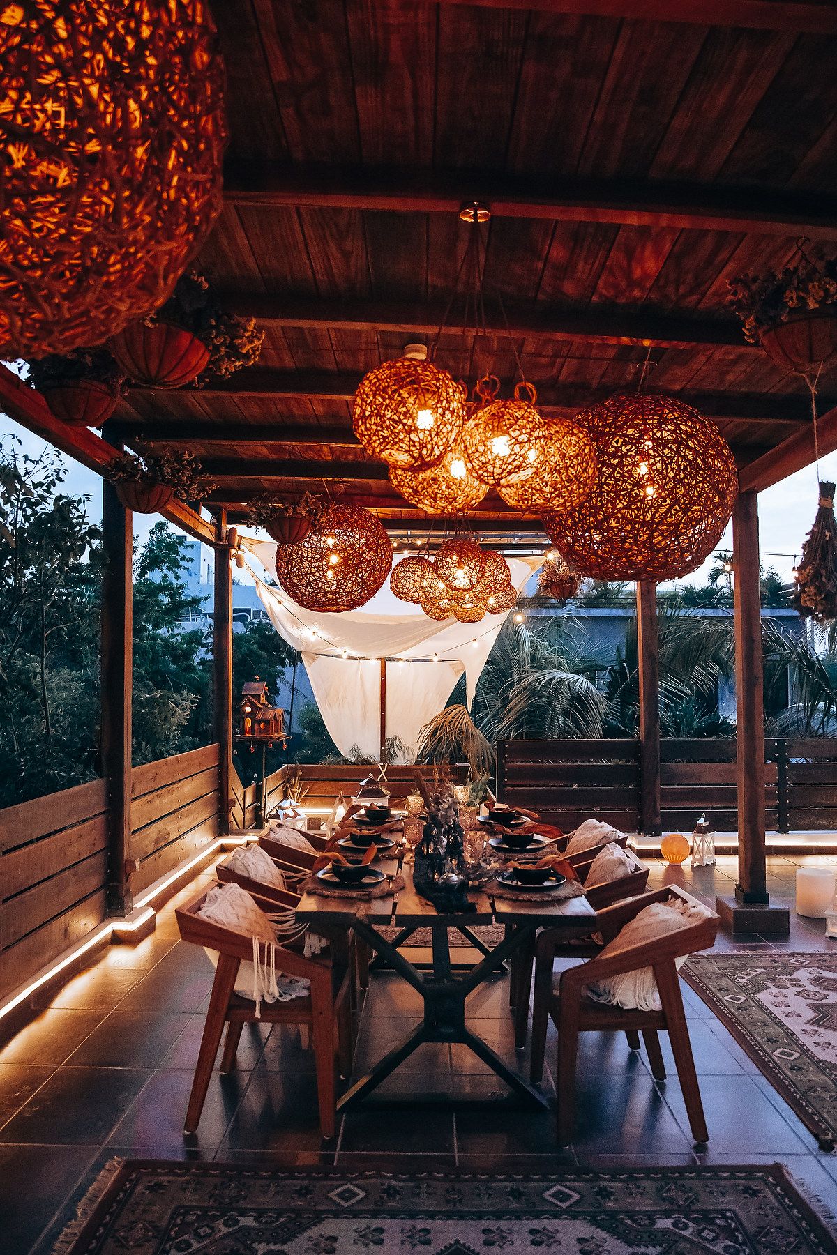 Cozy bohemian outdoor dining area with large woven rattan pendant lights and a set dinner table at dusk.