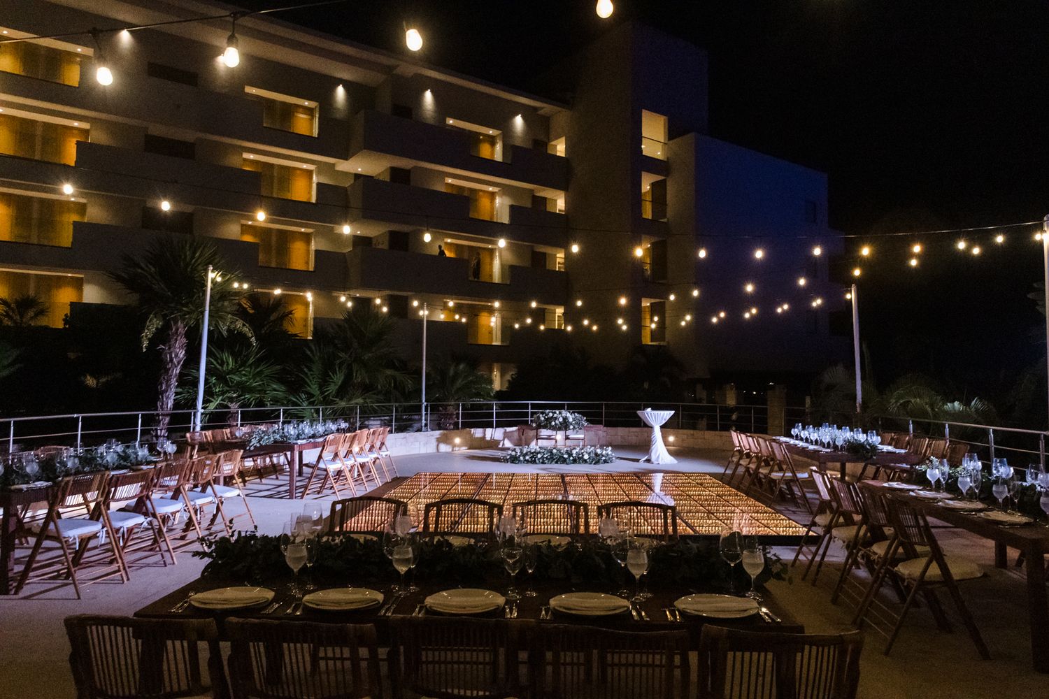 Elegant outdoor wedding reception at night with string lights and long dining tables set up on a hotel terrace.