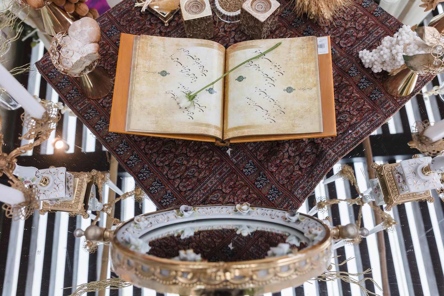 Ancient open manuscript book displayed on ornate carpet with decorative golden chandeliers and floral arrangements.