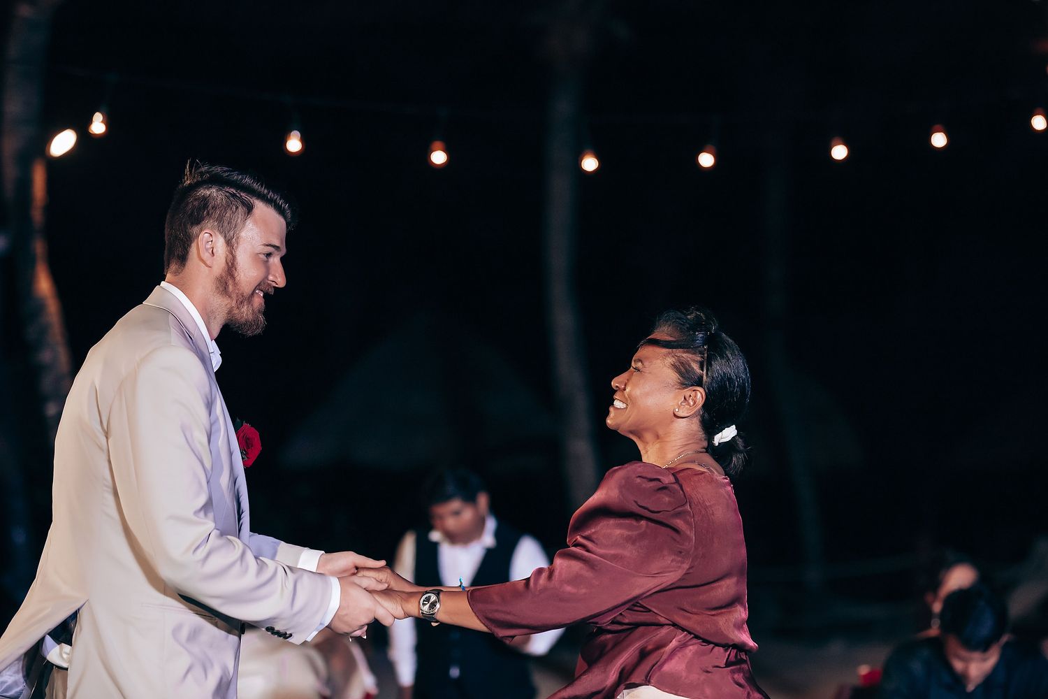 Wedding reception scene with string lights and dancing guests in evening setting.