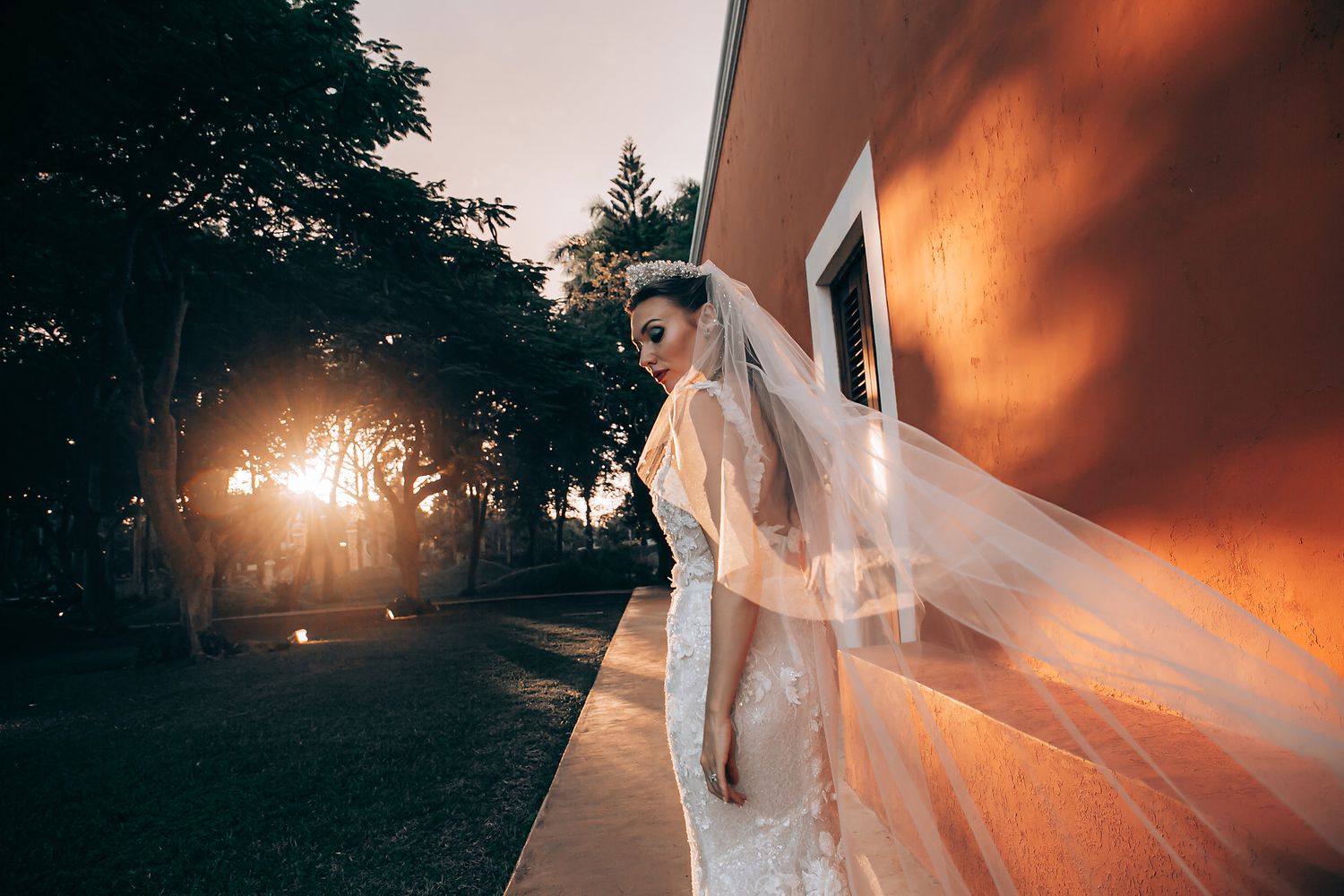 A romantic sunset wedding photoshoot with a flowing veil catching the golden light through trees.