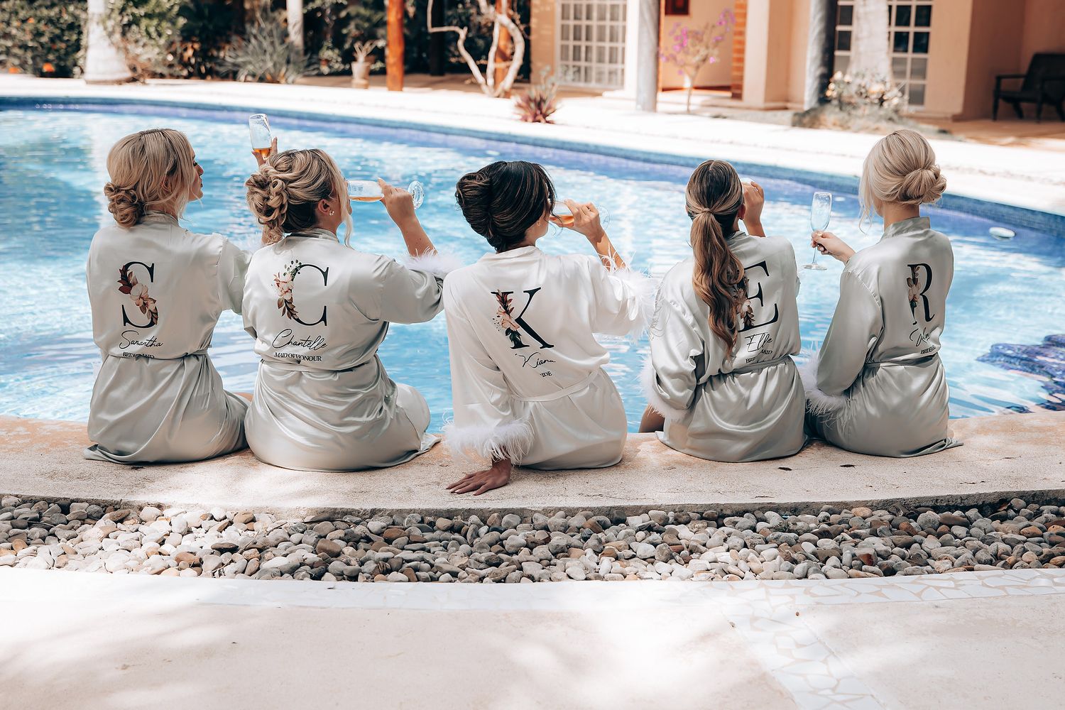 Five people in matching gray robes sitting by the edge of a pool with their backs to the camera.