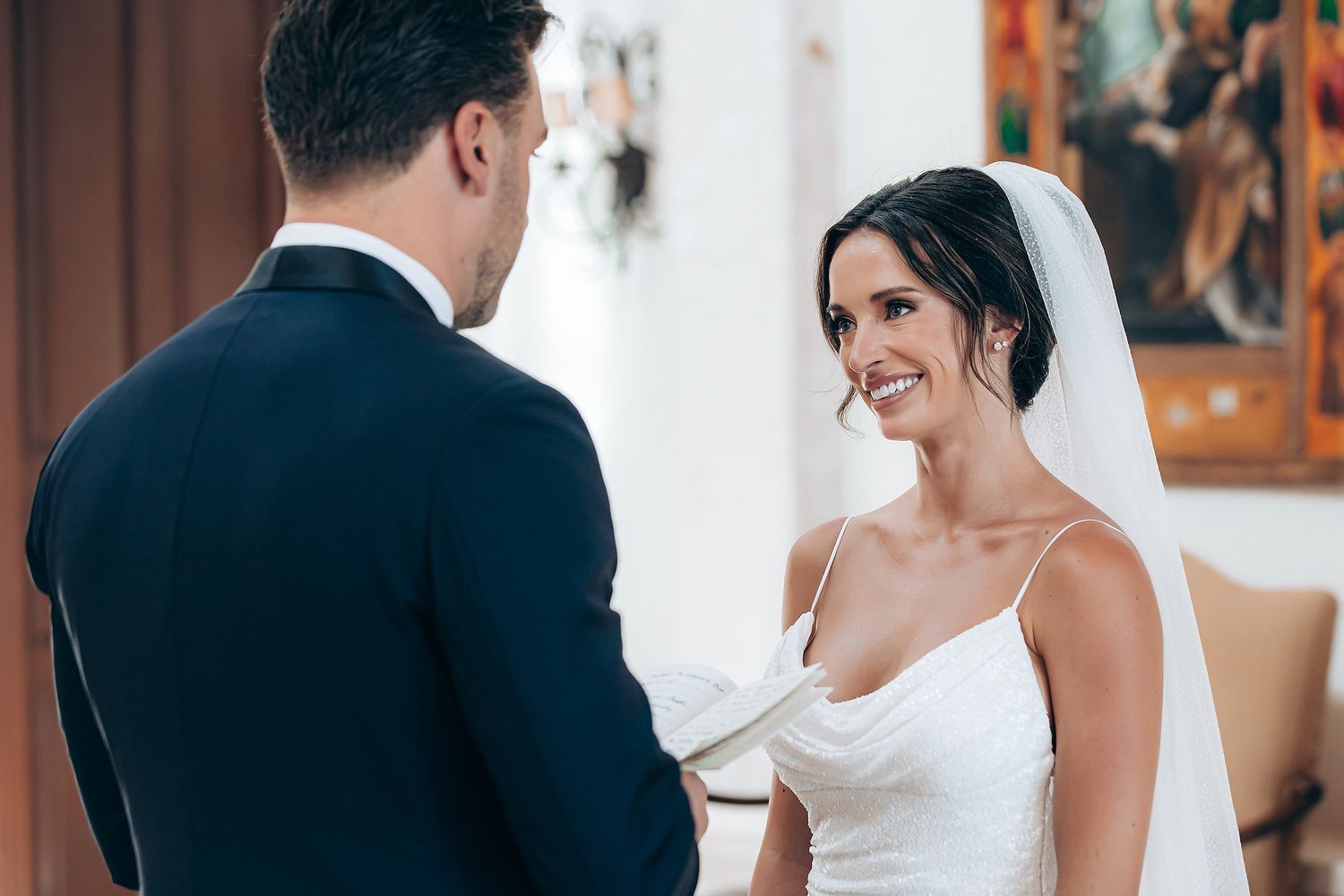 Wedding couple sharing an intimate moment in a grand white hallway with classical architecture.
