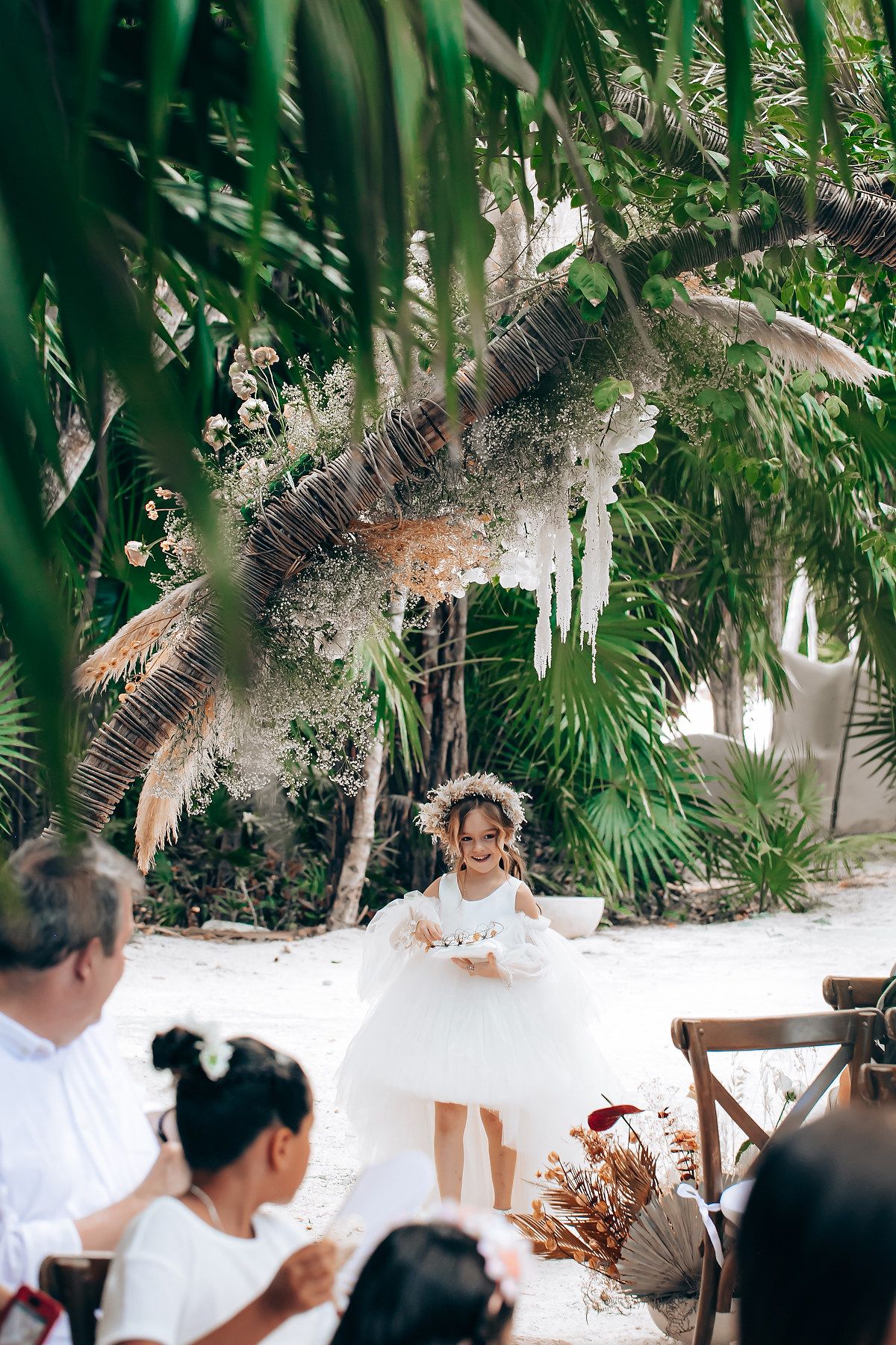 People in white attire gather at an outdoor tropical venue with palm trees and natural decor.