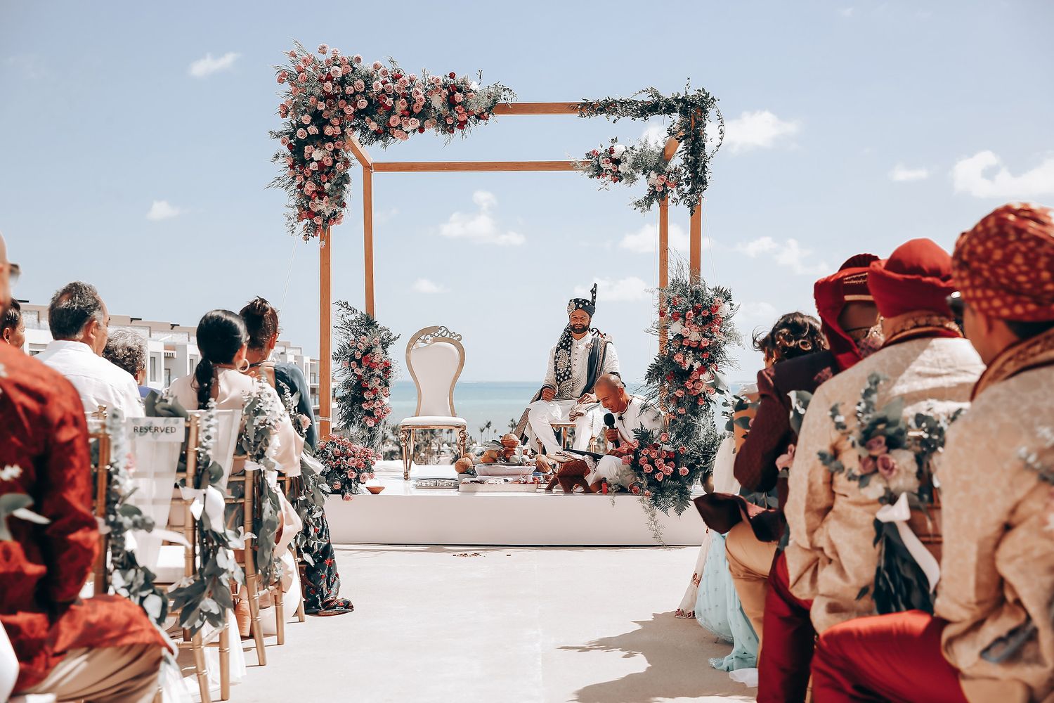 Beachside wedding ceremony setup with wooden arch and scattered guests.