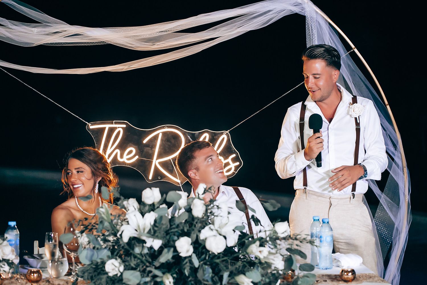 Wedding reception table decorated with white floral arrangements and flowing fabric.
