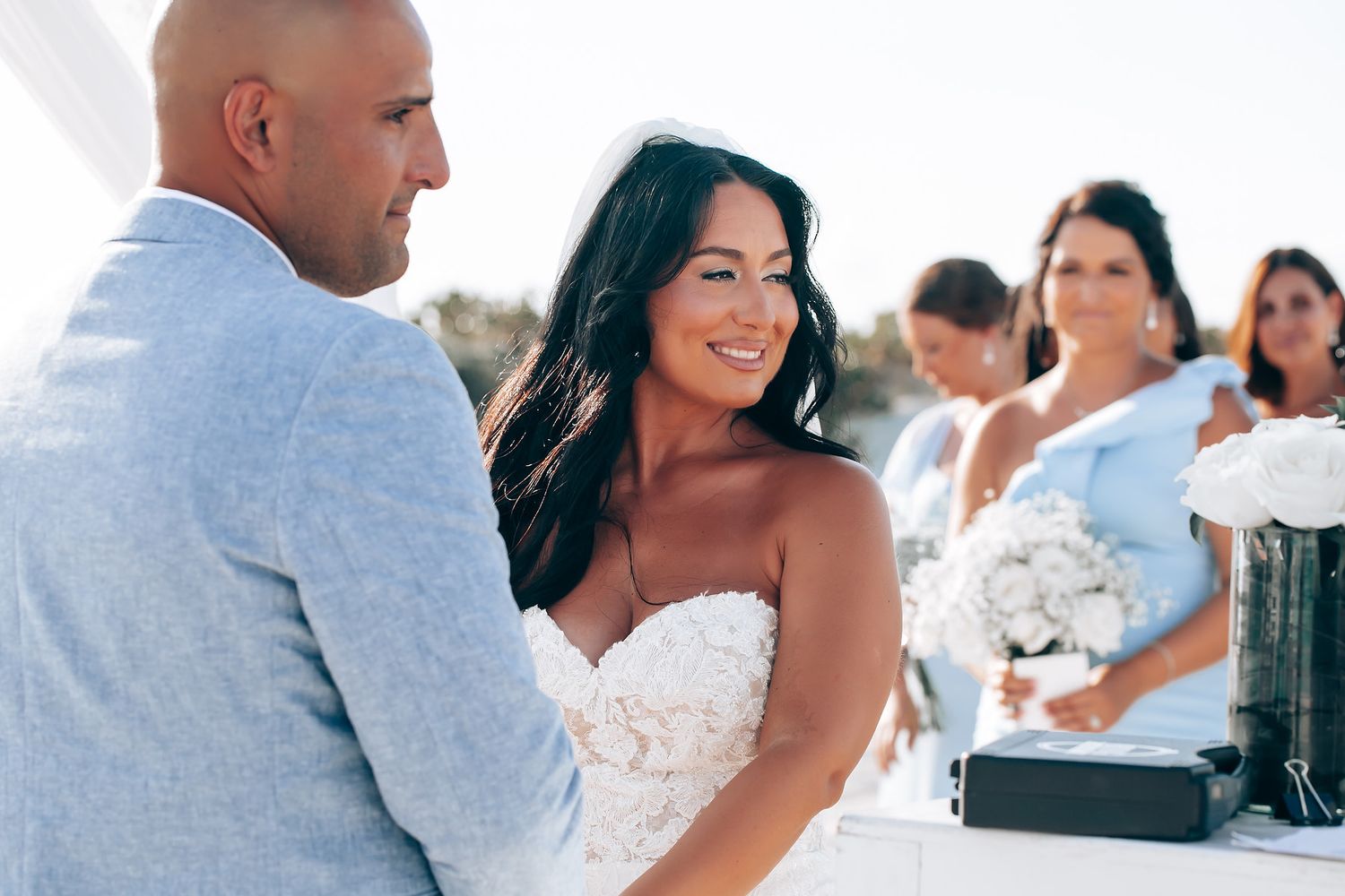 Candid wedding moments captured on a bright beach with guests in the background.